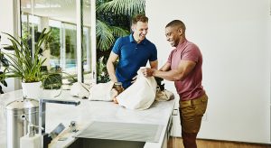 Smiling gay couple unloading groceries from canvas bags in kitchen
