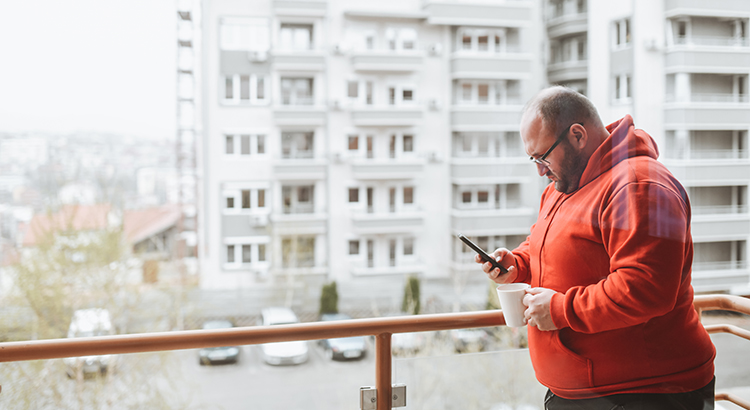 Bald Male Drinking Coffee On Balcony And Using Smartphone
