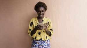 one young woman in front of pink wall smiling on mobile phone
