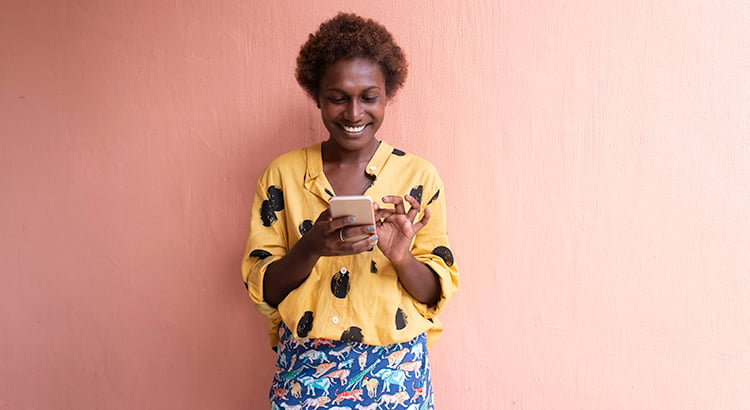 one young woman in front of pink wall smiling on mobile phone
