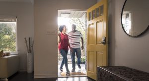 Young man and woman stepping into the house, they are happy and smiling as they come through the open yellow door