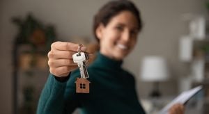Close up focus on keys, smiling woman realtor selling apartment, offering to client, showing at camera, holding documents, contract, making purchasing deal, real estate agent, mortgage or rent