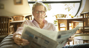 Smiling senior man in lounge room reading newspaper