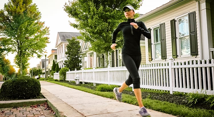 Young woman jogging in neighborhood with houses in the background.