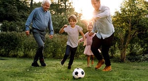 Full length of multi-generation family playing soccer in backyard
