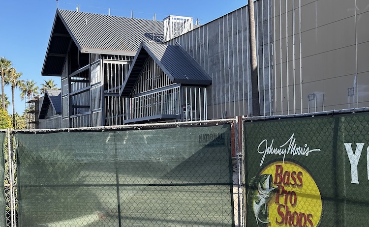 Construction fence in front of a building under construction. The sign on the fence reads Bass Pro Shops