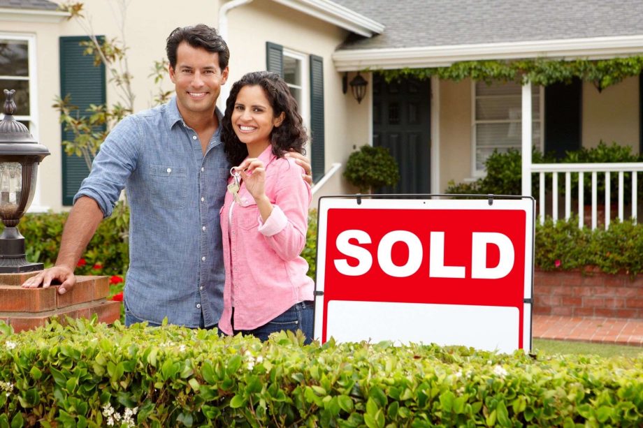 A happy couple in front of a home with a sold sign