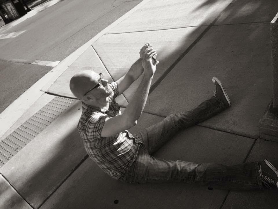 Tomi Kuczynski Sitting On Street next to Sidewalk Taking Picutre
