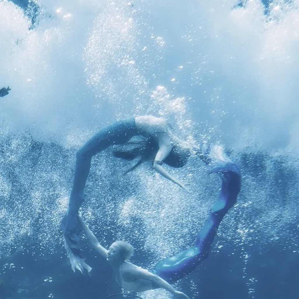 Weeki Wachee Mermaids swimming in a circle in aqua blue water.