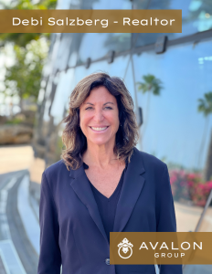 Debi Saltzberg St Pete Beach Realtor Is in the picture wearing a modern black suit. She is pictured in front of windows that are reflecting Palm Trees.