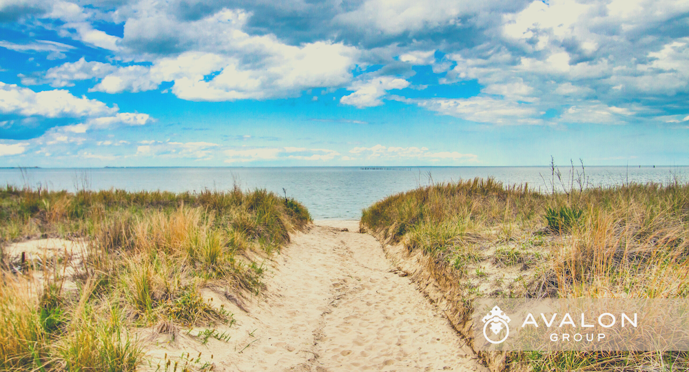 How do I Sell a Piece of Property in Florida? This picture shows a path to the beach flanked with sea grasses. The water is blue and there are puffy clouds that are white and gray.
