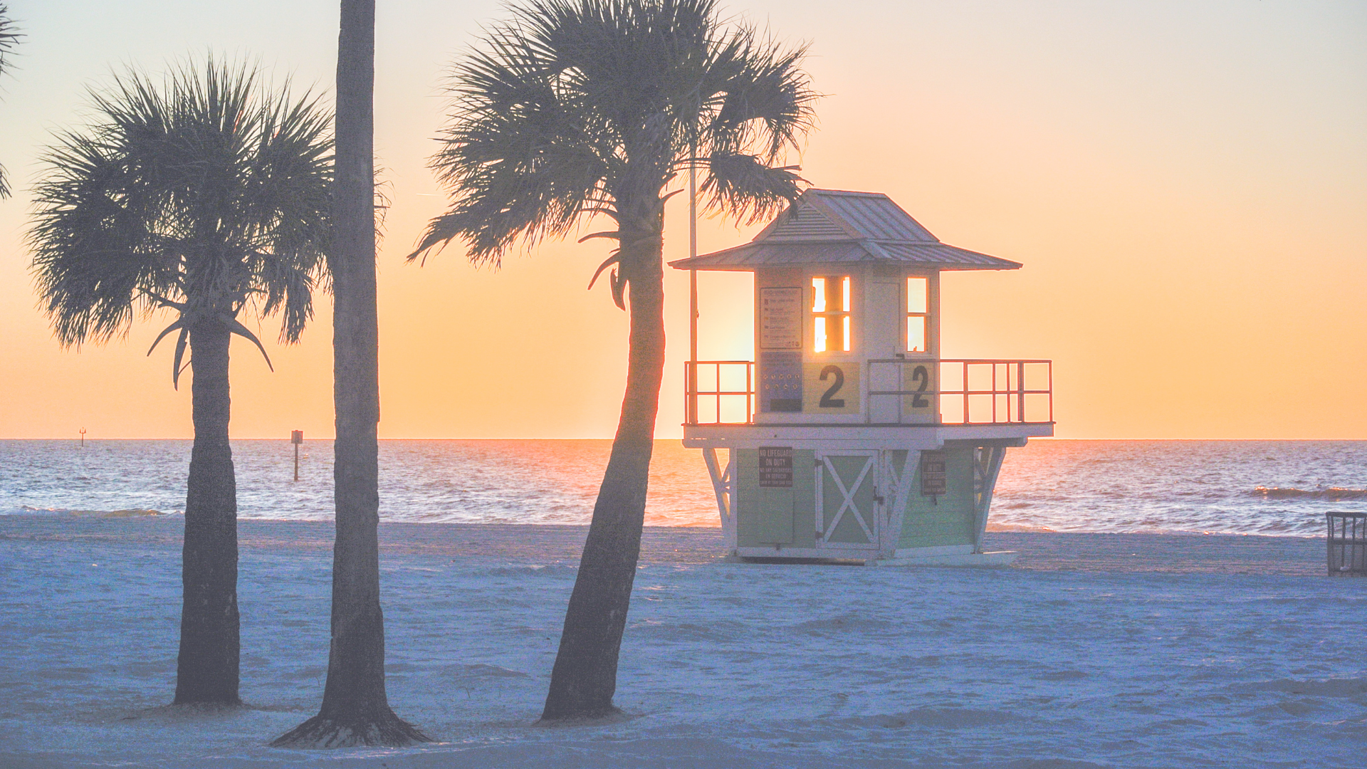Which Beach is Better St Pete or Clearwater: Picture shows Clearwater Beach at Sunset with the lifeguard stand surrounded by palm trees.