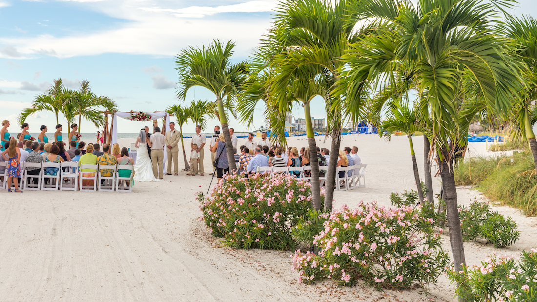 St Pete Beach is a popular place for weddings. In the picture is a wedding on the beach taking place with palm trees surrounding the event.