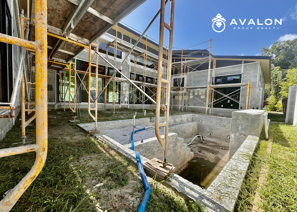 The pool courtyard will feature off-white beige colors with a raw concrete gray feature wall all in the picture. There is yellow scaffolding surrounding the walls.