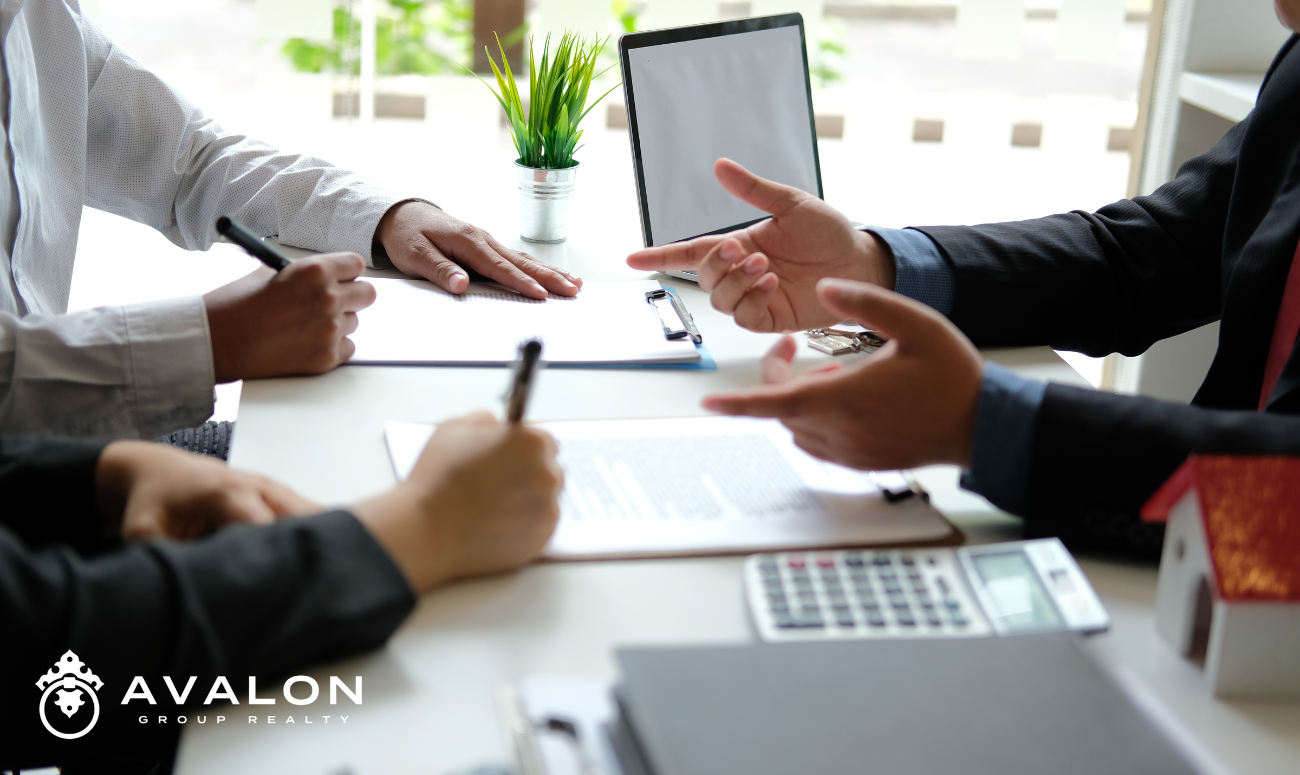This picture shows a desk view of the hands of the realtor and home sellers while deciding on the best price for their home.