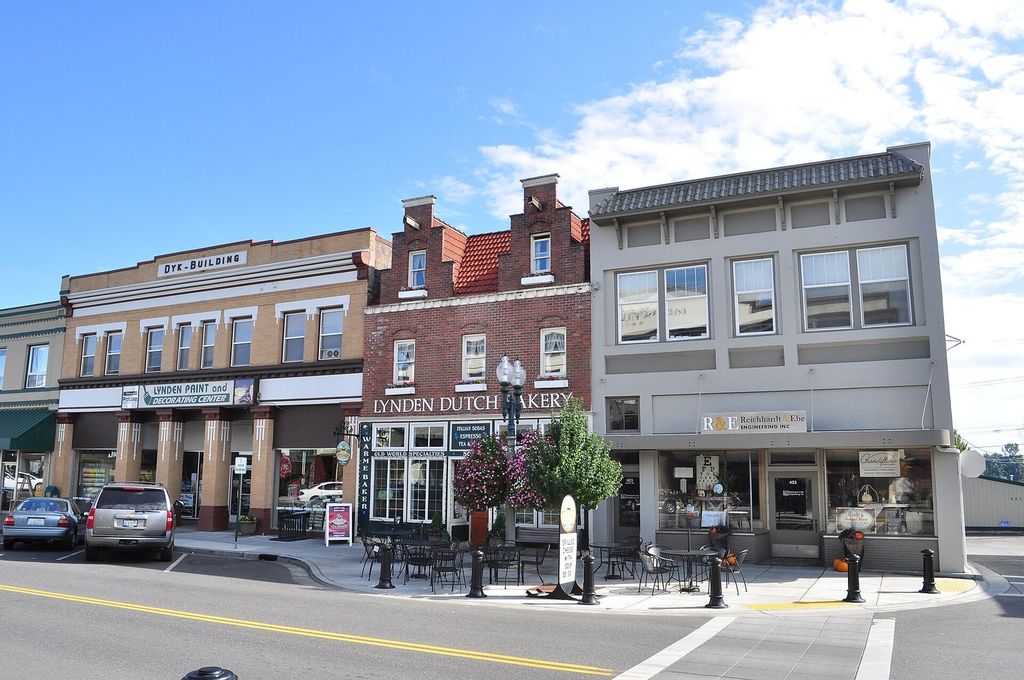 Historic brick and stucco storefronts on Front Street in downtown Lynden, with outdoor café tables and hanging flower baskets on the sidewalk