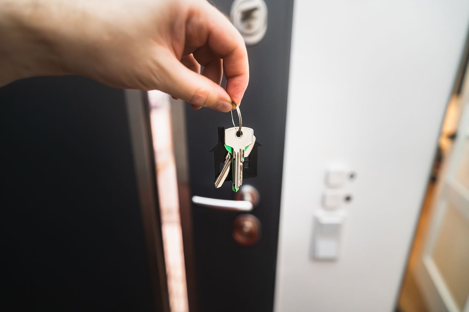 Hand holding house keys in front of an open front door