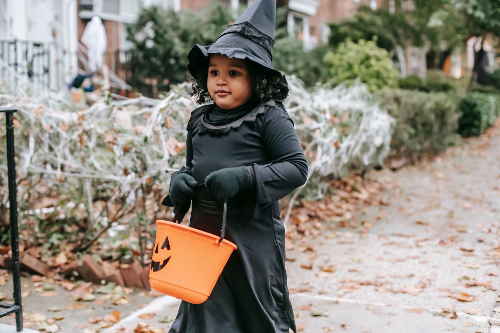 Child in witch costume with pumpkin bucket outdoors