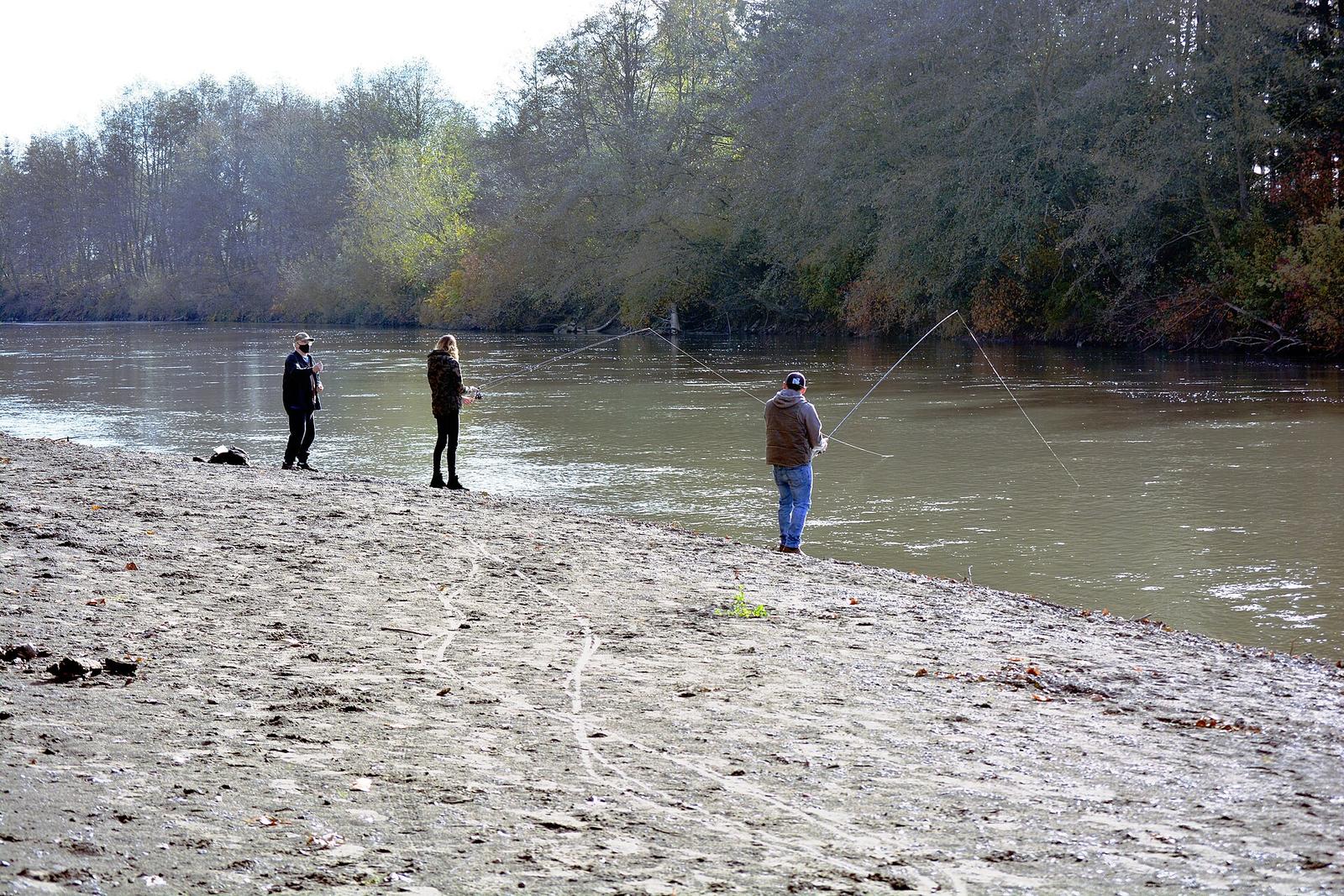 People fishing from a gravel bar on the calm Nooksack River at Hovander Homestead Park in Ferndale, with fall trees on the far bank