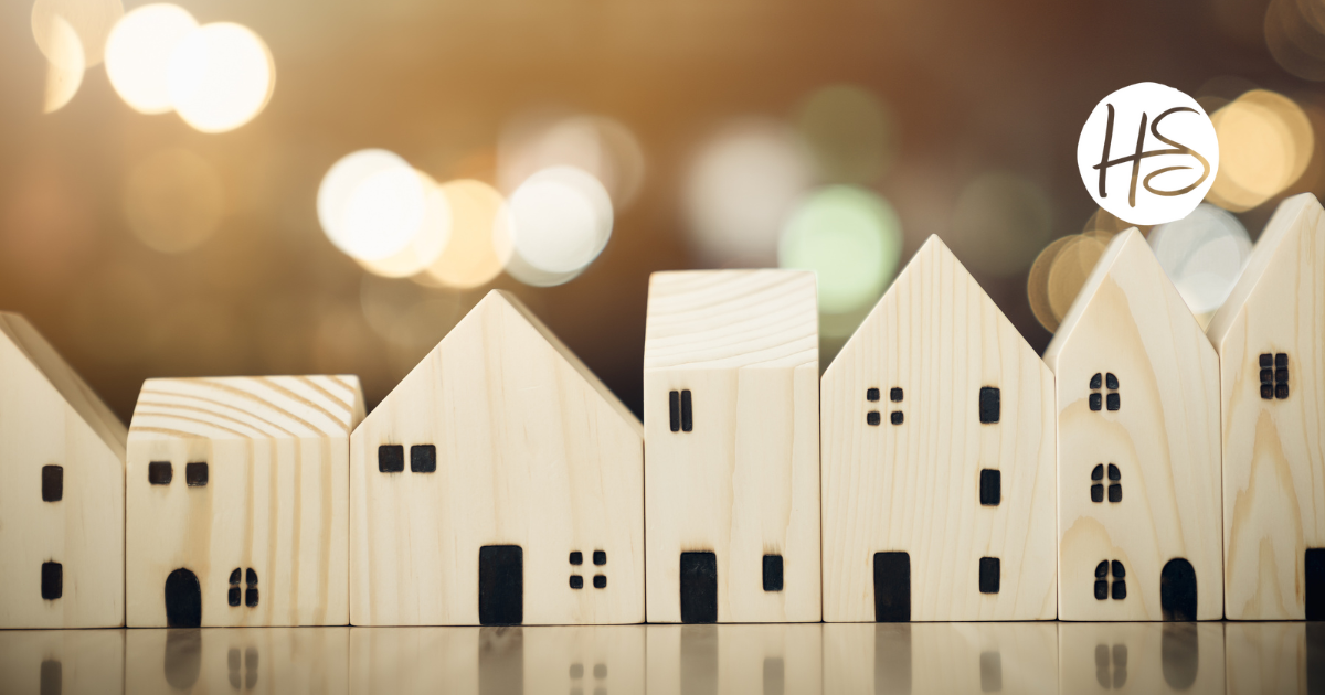 Row of minimalist wooden house models against a blurred, warm-toned background with the HomeSource Realty logo in the upper right corner