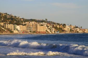 A panoramic view of Main Beach showing the boardwalk, volleyball courts, and lifeguard tower surrounded by oceanfront homes — ideal for highlighting Laguna Beach real estate and lifestyle.