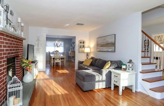 Bright and welcoming living room with hardwood floors, a brick fireplace, and abundant natural light.