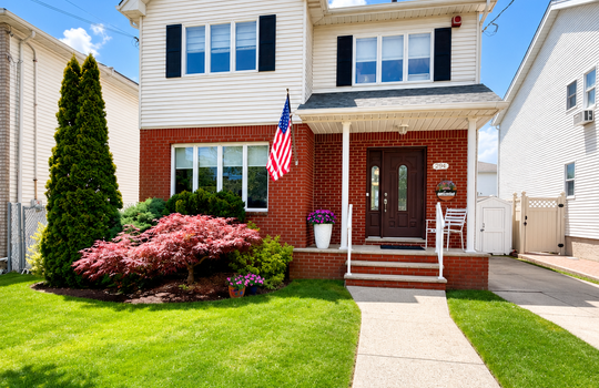 Front exterior of a two-story colonial home with brick facade, covered front porch, private driveway, and manicured front lawn in Tottenville, Staten Island.