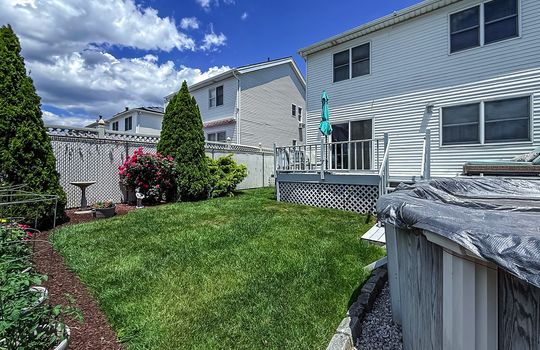 Private fenced backyard with manicured lawn, elevated deck, mature landscaping, and above-ground pool in a Tottenville Staten Island home minutes from the Conference House.
