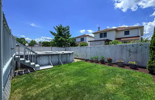 Rear yard with deck, above-ground pool, grass lawn, and privacy fencing behind a two-story home.