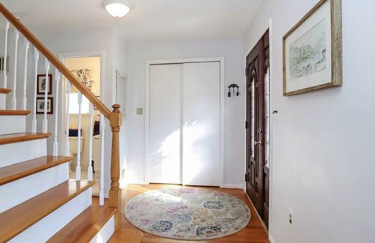 Spacious entry foyer featuring hardwood flooring, convenient closet storage, and an elegant staircase