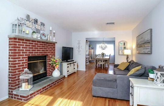 Sun-filled living room featuring hardwood floors, a wood-burning brick fireplace, and an open-concept flow to the dining room in this Staten Island home for sale.