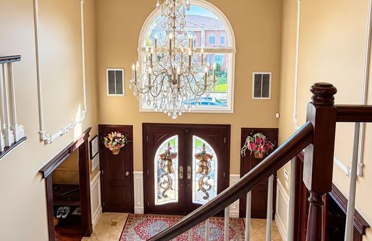 Elegant two-story foyer featuring a crystal chandelier, ornate ceiling medallion, decorative wall moldings, hardwood staircase, and double entry doors.