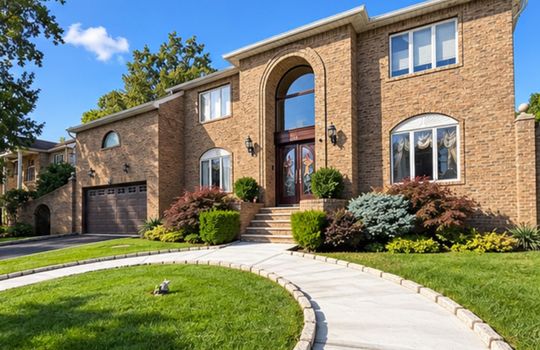 Beautiful two-story brick home with grand arched entrance, landscaped front lawn, curved walkway, and attached garage in Staten Island, NY.