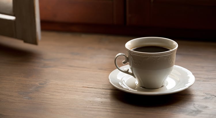 One glass of black tea, chicory or coffee on a light wood table, on a window sill near a window, in a cafe, cafeteria or at home. The concept of loneliness, breakfast. Coffee break. A copy of the space.