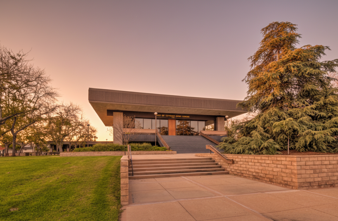 Photorealistic image of the City of Cypress Civic Center in California, captured in warm late afternoon sunlight with stairs, trees, and landscaped grounds in view.