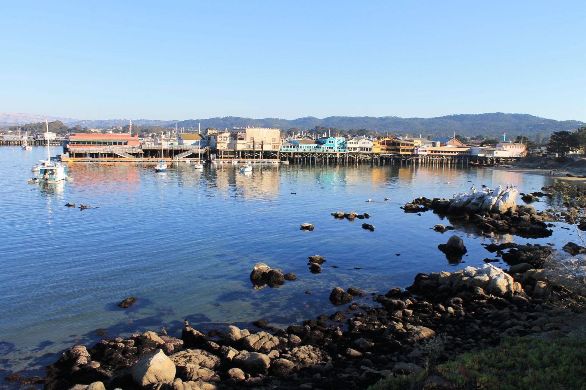 Colorful shops along Old Fisherman’s Wharf on Monterey harbor, with boats and rocky shoreline