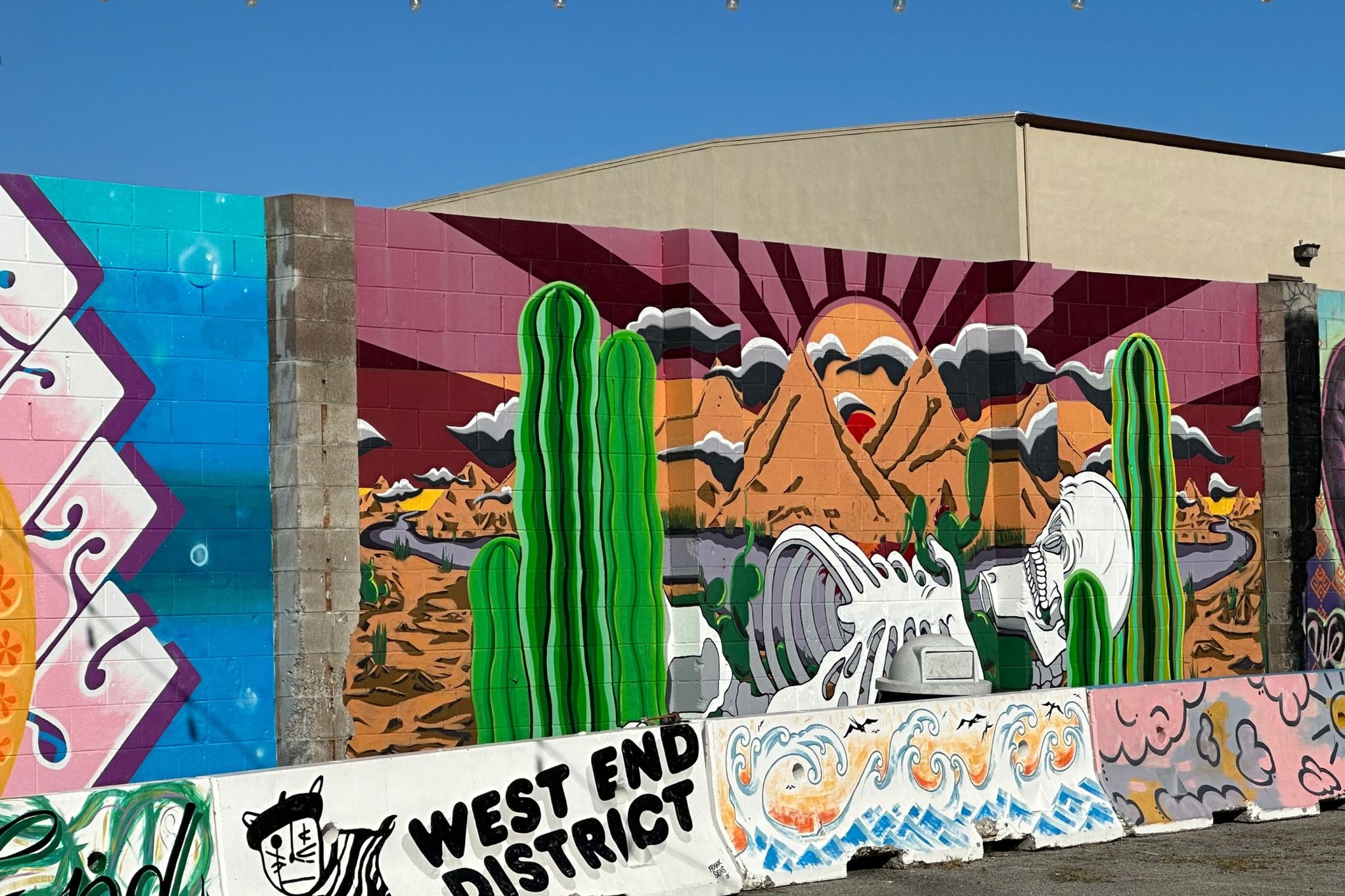 Colorful murals of cactus, mountains and a crashing wave on a block wall in the West End District of Sand City