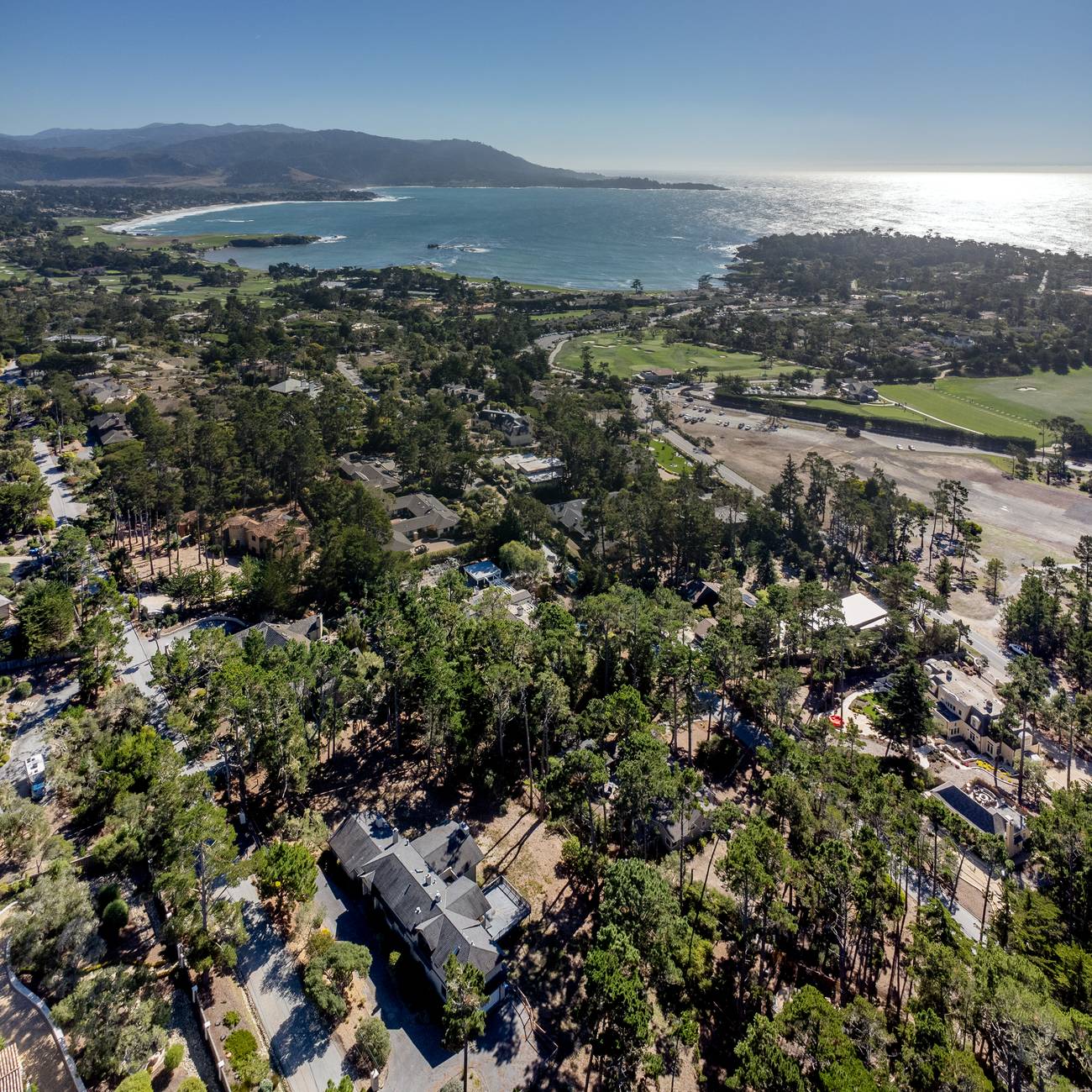 Aerial view of 1424 Oleada Road in Pebble Beach among Monterey pines, with Carmel Bay and the golf links beyond