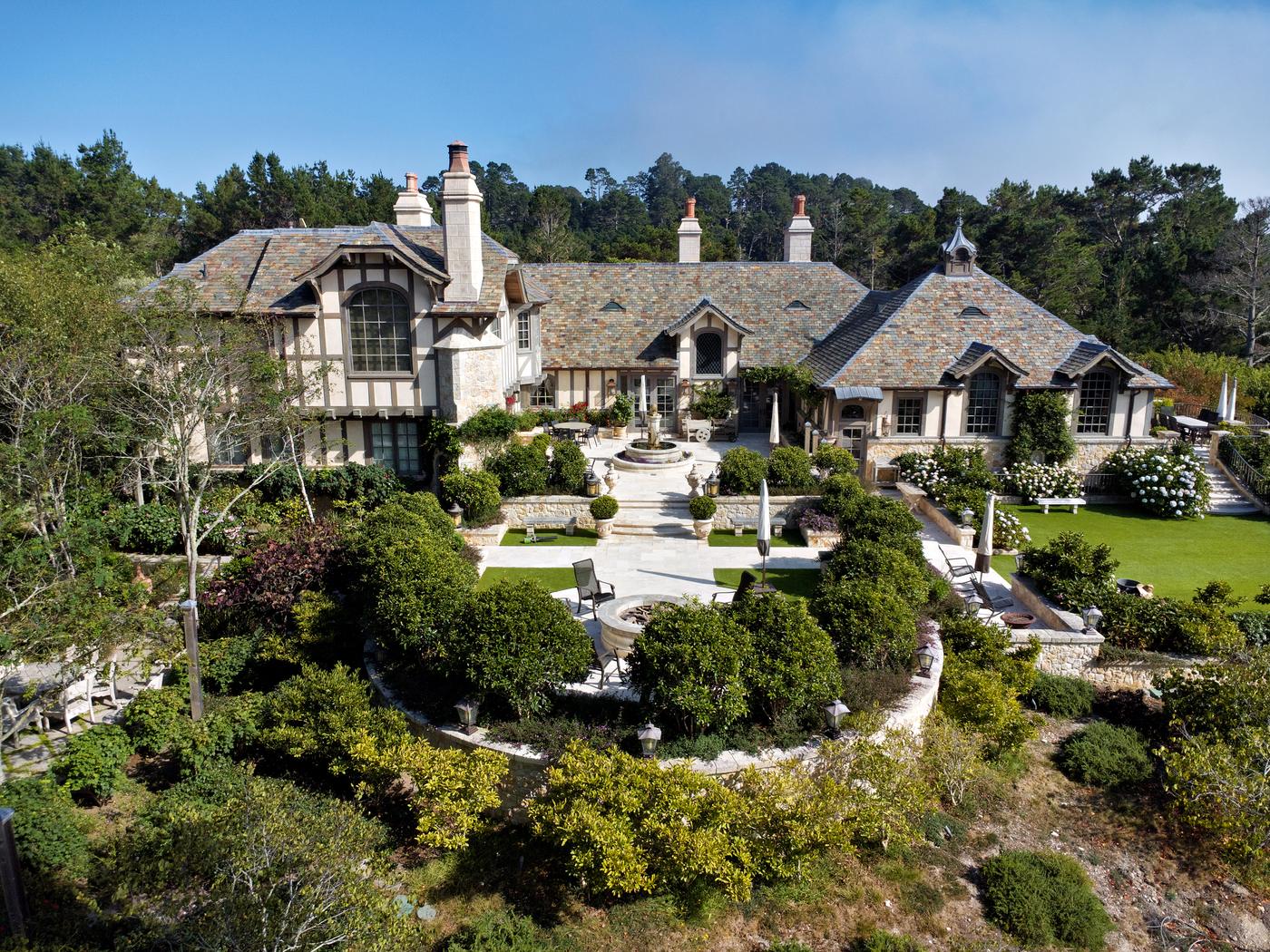 Aerial view of 2 La Pradera Lane, a Tudor-style estate with stone chimneys and terraced gardens in Carmel