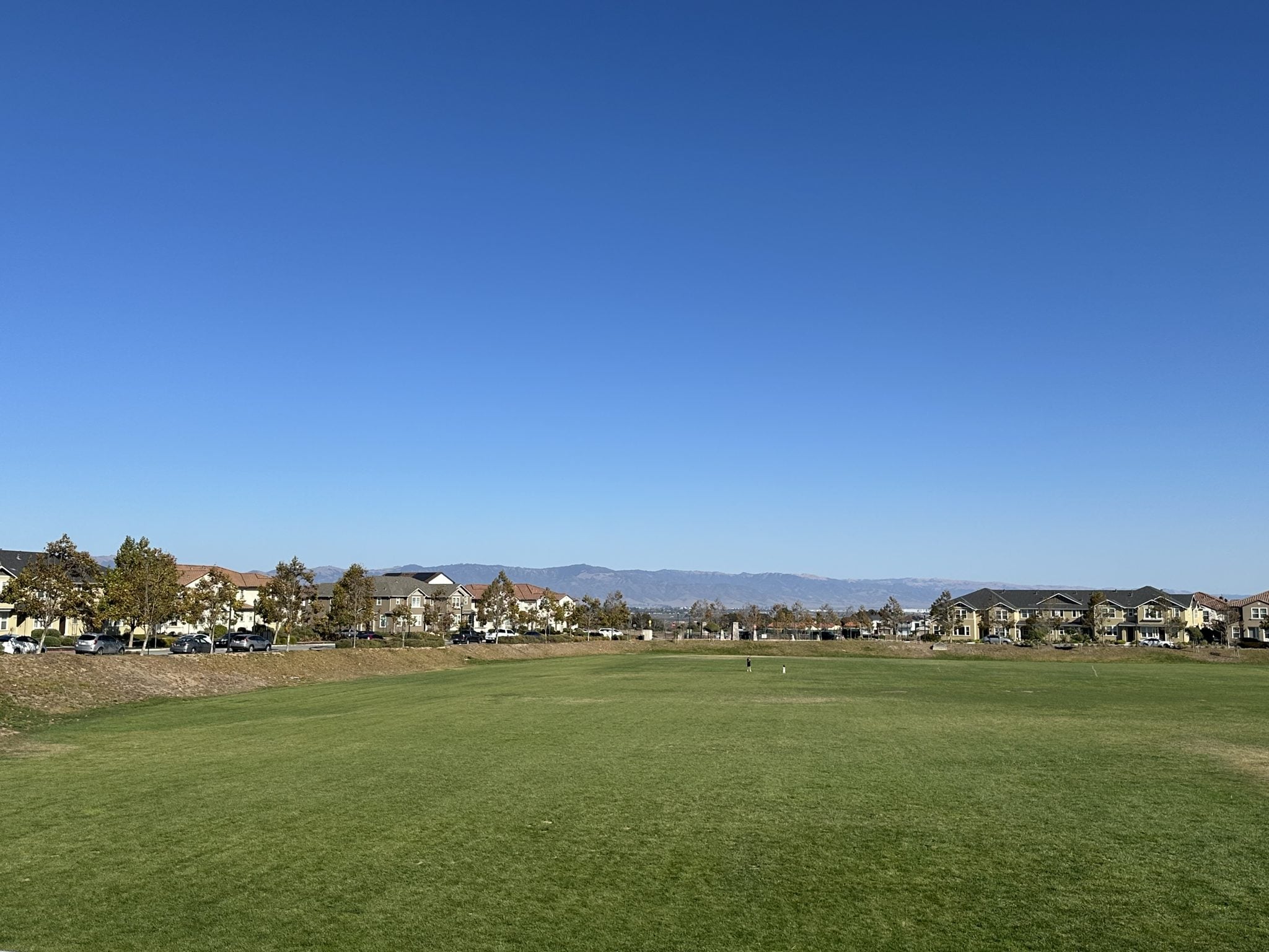 A park lawn in East Garrison with homes and mountain views under a clear sky