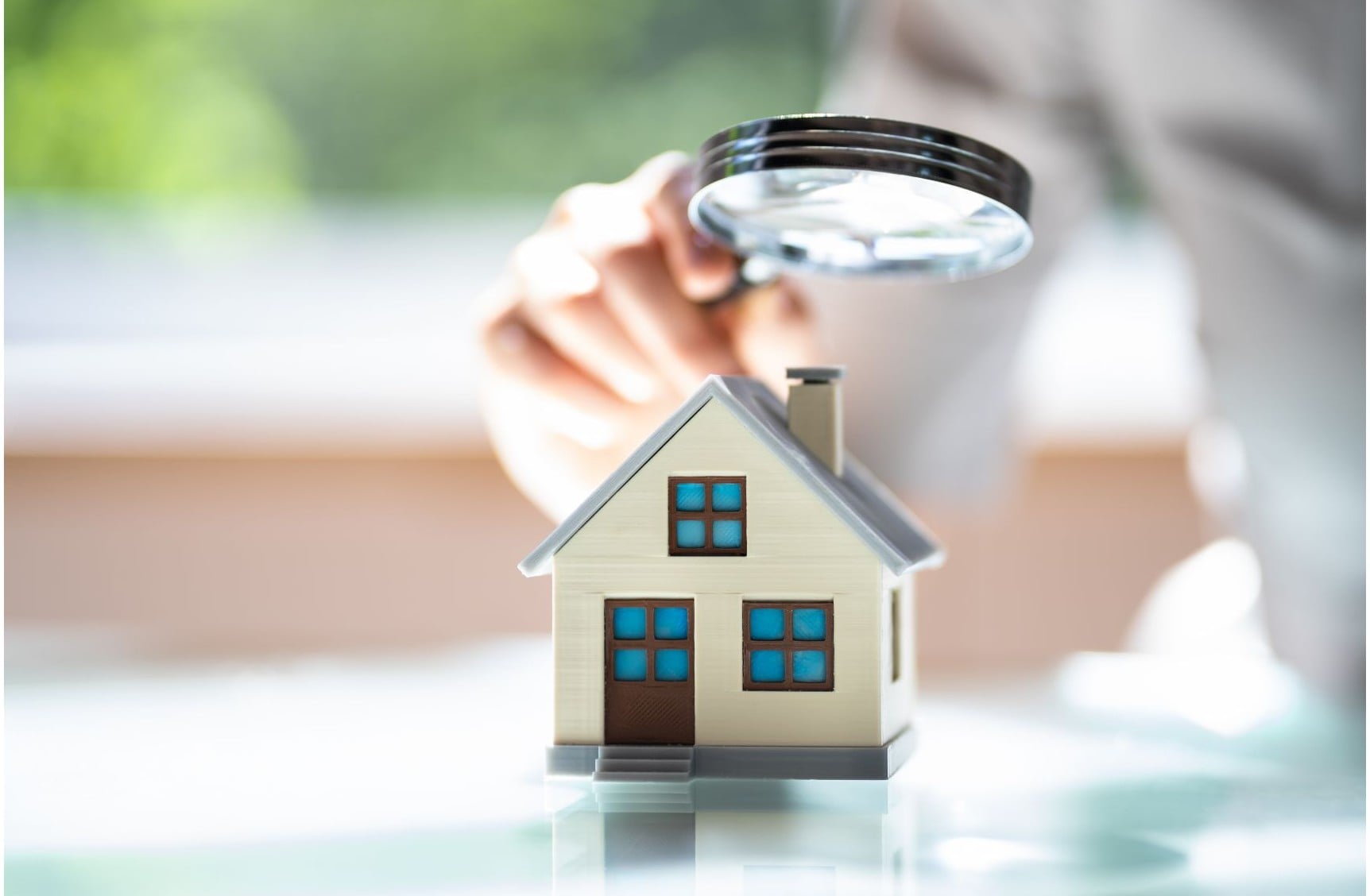 Magnifying glass held over a small model house, representing a detailed home appraisal review