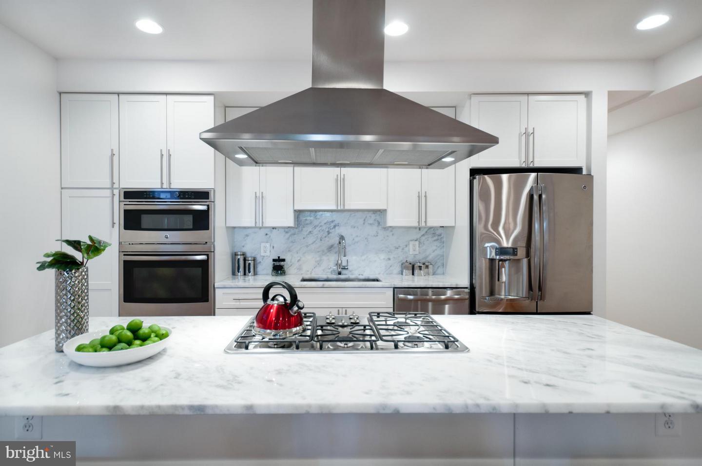 Photograph - Modern kichen with white cabinets and stone countertops, a drop-down exhaust vent and a gas cooktop