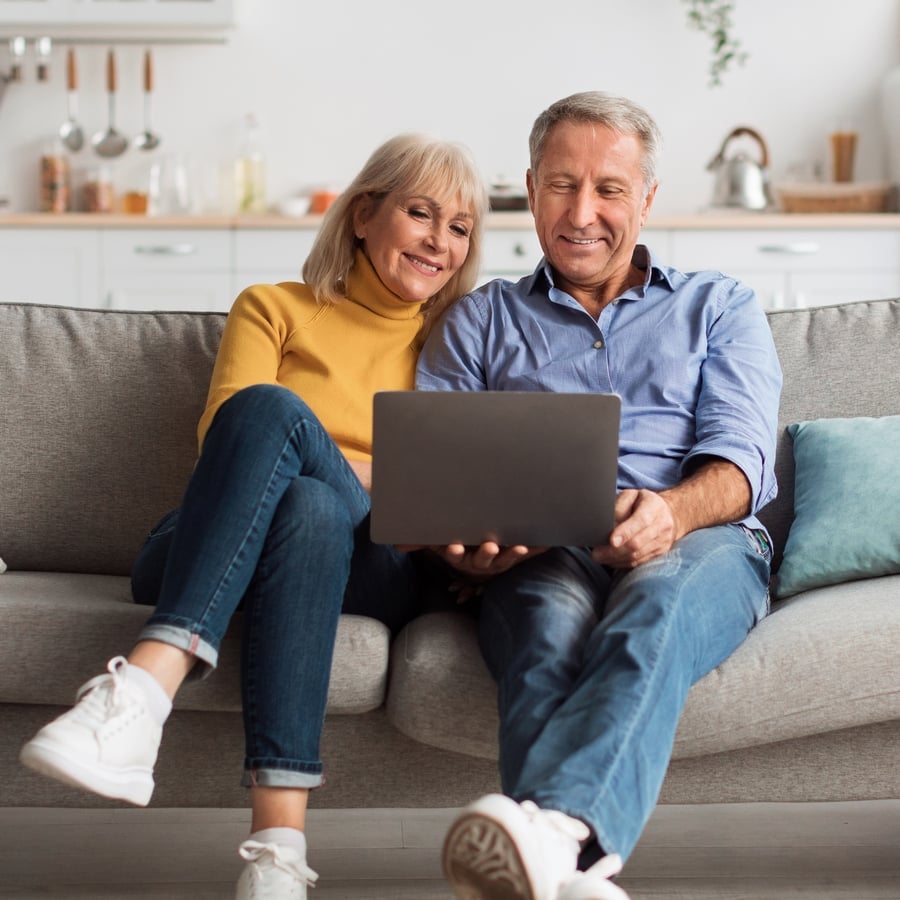 Senior,Spouses,Using,Laptop,Watching,Movie,Together,Sitting,On,Couch