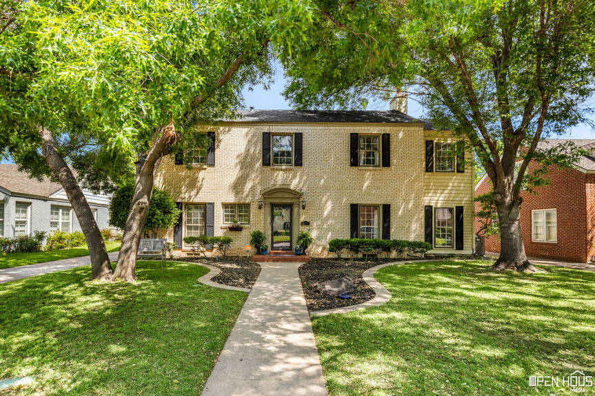 Front view of a two-story Colonial-style home with a brick walkway, green lawn, and mature trees.