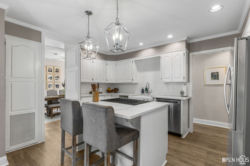 A view into the kitchen showcasing white cabinetry, modern lighting, and gray upholstered bar stools.