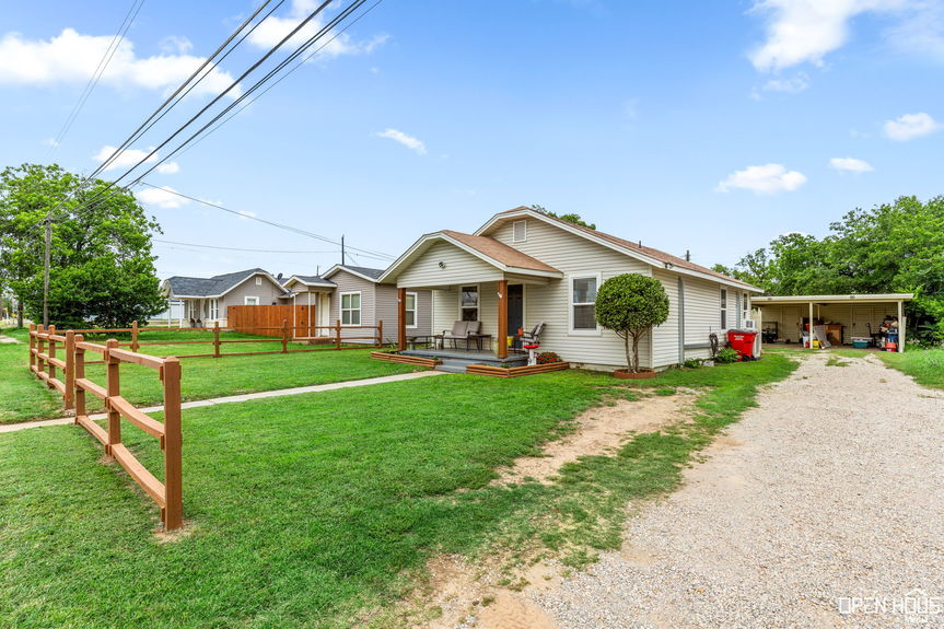 View of a single-story house with a beige exterior, front porch, and a neat lawn bordered by a wooden fence.