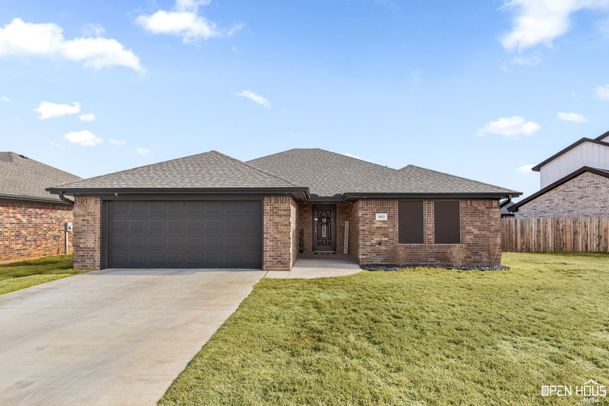 Exterior view of a single-story brick home with a dark garage door, driveway, and front lawn under a clear blue sky.