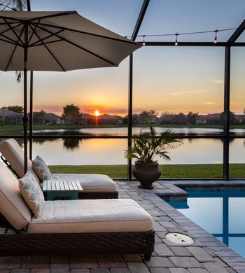 Florida screened swimming pool with lounge chairs overlooking lake at sunset