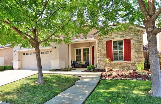 A single-story house with a stone facade, bright red window shutters, a front porch with chairs | Loomis Real Estate