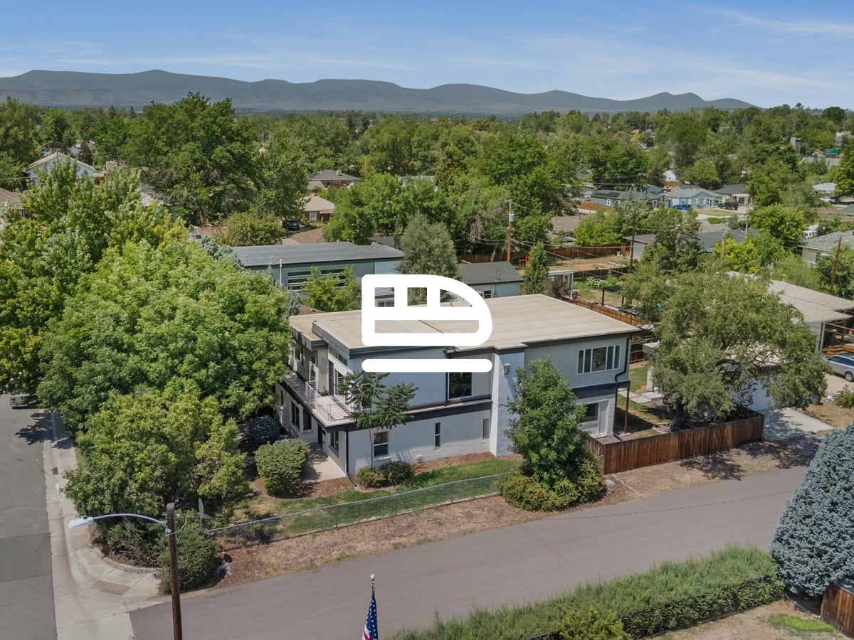 Aerial view of a modern two-story home on a tree-lined street with mountains on the horizon